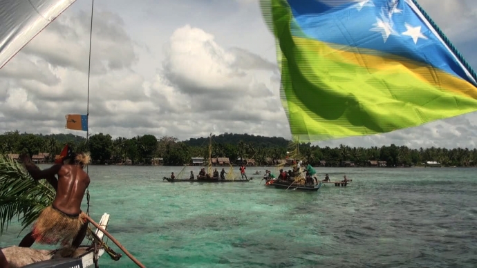 Climate Challenger flying the Solomon Island flag, cruises into Pere village after their 3 month long distance voyage. (photo: taken as a still from video)
